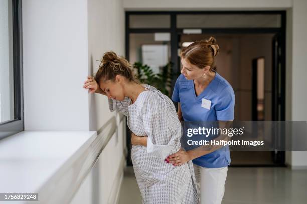 nurse helping pregnant woman with painful labour contractions in the hospital hall. woman in labor, dressed in hospital gown doing breathing exercises, deep breathing to relieve pain. - midwife stock pictures, royalty-free photos & images