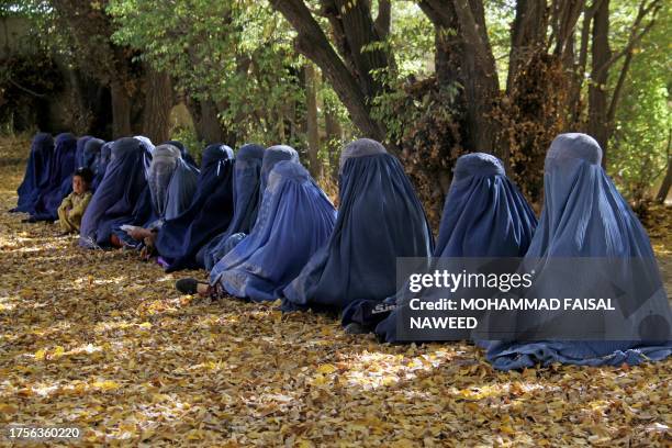 Afghan burqa-clad women sit as they wait to receive cash money from the United Nations High Commissioner for Refugees , in Ghazni on October 31, 2023.