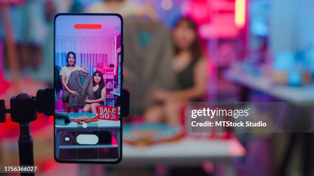 primer plano de mujeres asiáticas jóvenes transmitidas en vivo por teléfono muestran ropa de moda de nueva colección al cliente en la tienda por la noche. comercio electrónico pyme para pequeñas empresas. - grabado objeto fabricado fotografías e imágenes de stock
