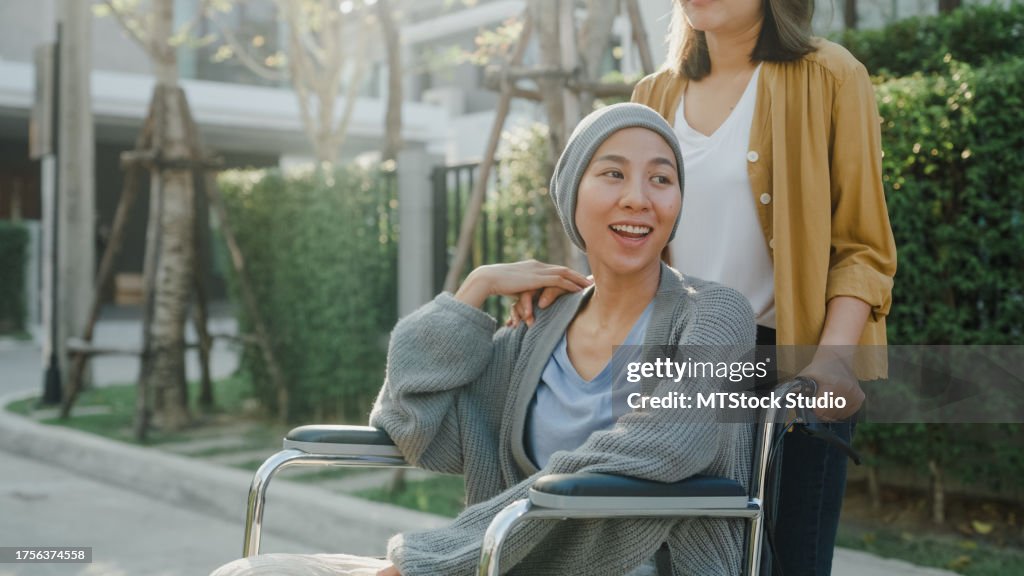 介護医療を受けているアジアの若者は、家の外で車椅子に座っているがん患者を助けます。医療。