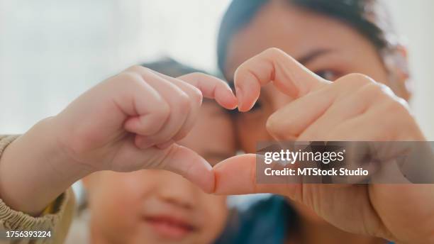 gros plan d’un jeune enfant d’une famille asiatique faisant des signes en forme de cœur sur un canapé dans le salon à la maison. amour montrant le geste du cœur de la main, moment heureux en famille. - adoption photos et images de collection
