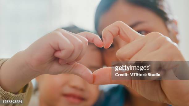 closeup of young asian family child making fingers heart shaped signs on sofa in living room at home. love showing hand heart gesture, family happy moment. - adoption stock pictures, royalty-free photos & images