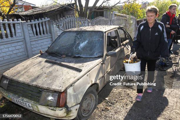 Woman carries a bucket past a damaged car after falling debris from downed Russian rockets landed in Dnipro district, Dnipropetrovsk Region, central...