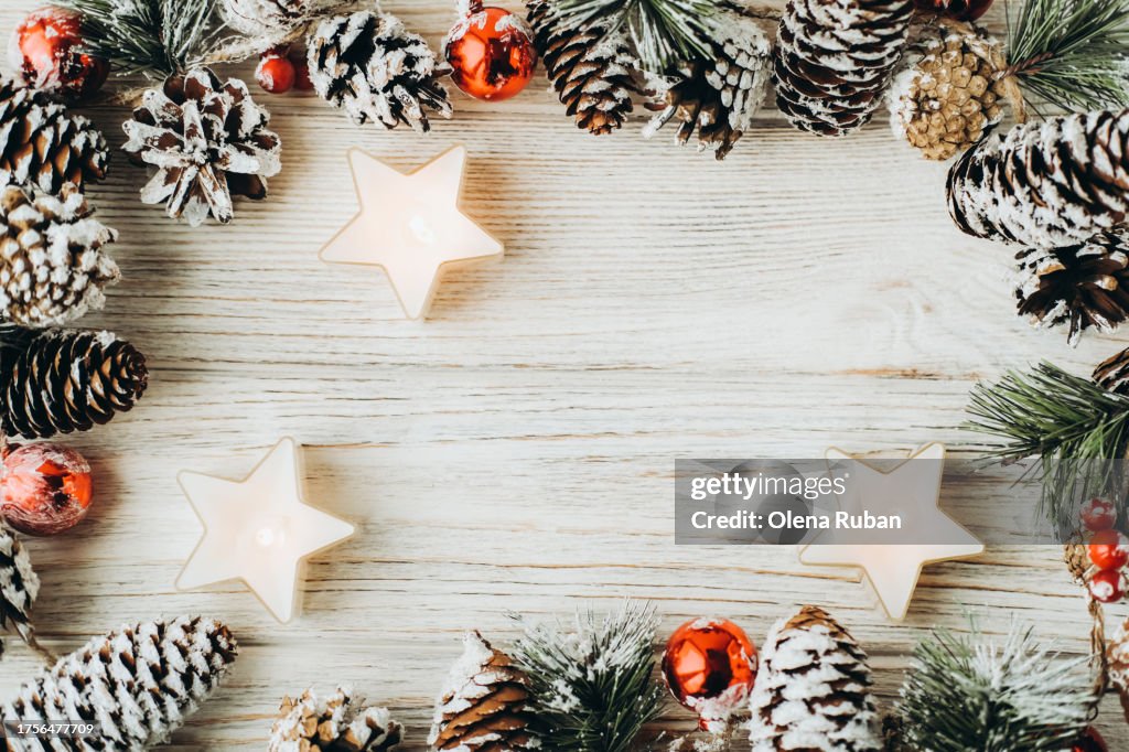 Star tealight candles among spruce branches with cones and berries on white wooden surface with space for text.