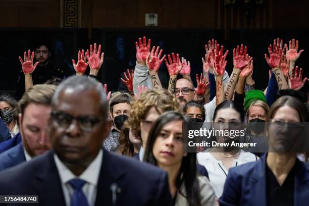 Secretary of Defense Lloyd Austin testifies as protestors calling for a ceasefire in Gaza raise their hands, painted in red, during a Senate...