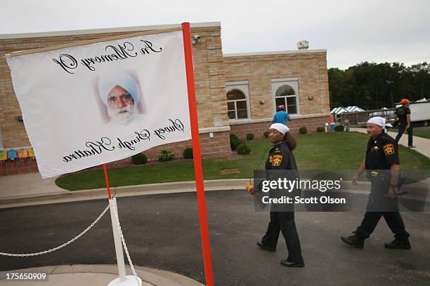 Police walk by a banner honoring one of the victims of the shooting at the Sikh Temple of Wisconsin during a service held to mark the one-year...