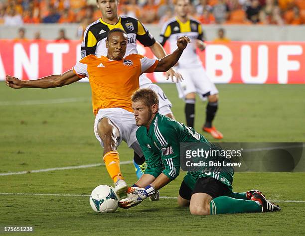 Matt Lampson of the Columbus Crew makes a save before Ricardo Clark of the Houston Dynamo can get his foot on the ball at BBVA Compass Stadium on...
