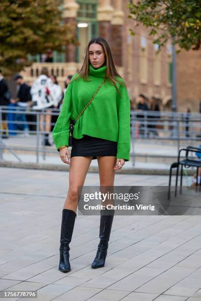 Guest wears green turtleneck, black mini skirt, black boots on day 2 of 080 Barcelona Fashion 2023 at Recinte Modernista de Sant Pau on October 25,...