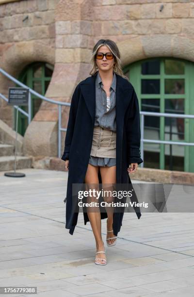 Guest wears grey button shirt, beige mini skirt, heels, black coat, sunglasses on day 2 of 080 Barcelona Fashion 2023 at Recinte Modernista de Sant...