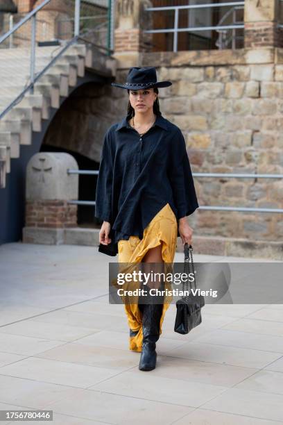 Guest wears cowboy hat, black button shirt, bag, yellow skirt with slit on day 2 of 080 Barcelona Fashion 2023 at Recinte Modernista de Sant Pau on...