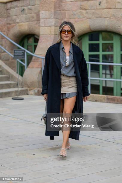 Guest wears grey button shirt, beige mini skirt, heels, black coat, sunglasses on day 2 of 080 Barcelona Fashion 2023 at Recinte Modernista de Sant...