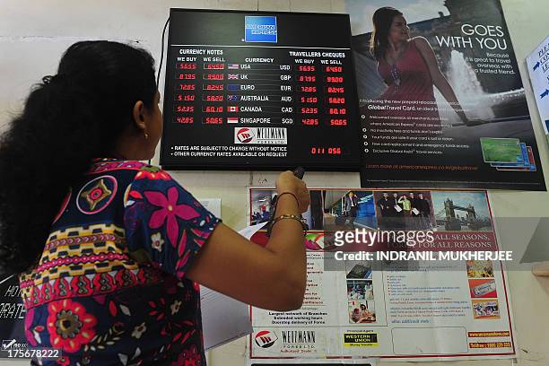 An employee works next to a board showing the exchange rate of Indian rupees to other currencies at a foreign exchange dealer in Mumbai on August 6,...