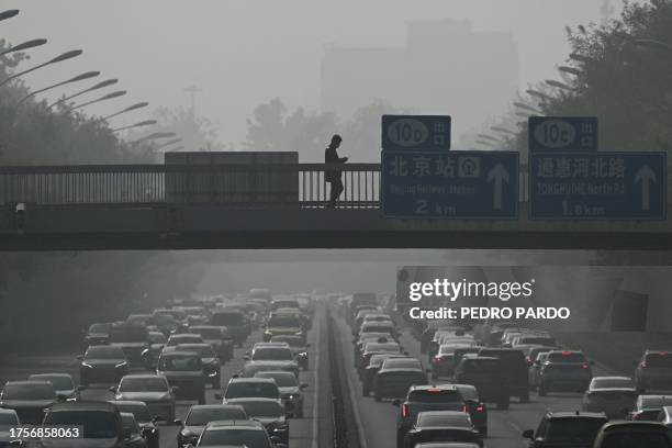 Pedestrians walk on an overpass as traffic snarls amid haze from air pollution in Beijing on November 1, 2023. A thick haze has smothered swathes of...