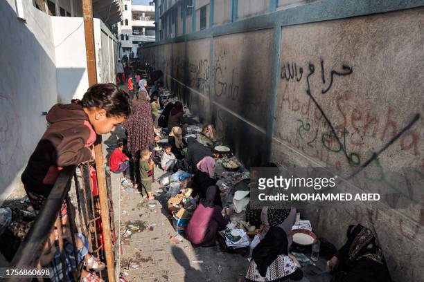 Children watch as women sit baking traditional flatbread along an alley in Rafah in the southern Gaza Strip on November 1, 2023 amid ongoing battles...
