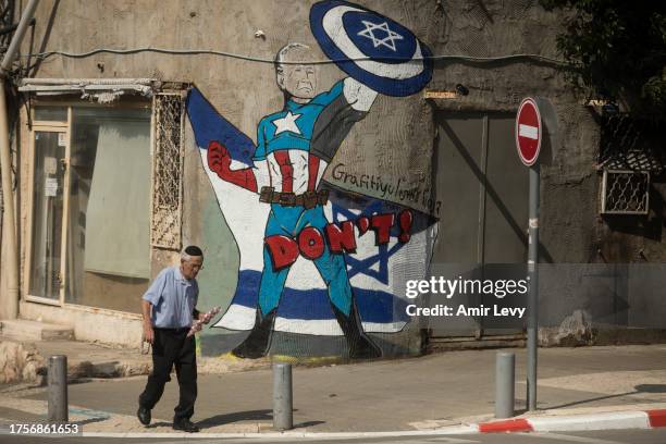 Man walks by street art showing US President, Joe Biden, as Captain America super hero on a street in southern Tel Aviv on November 01, 2023 in Tel...