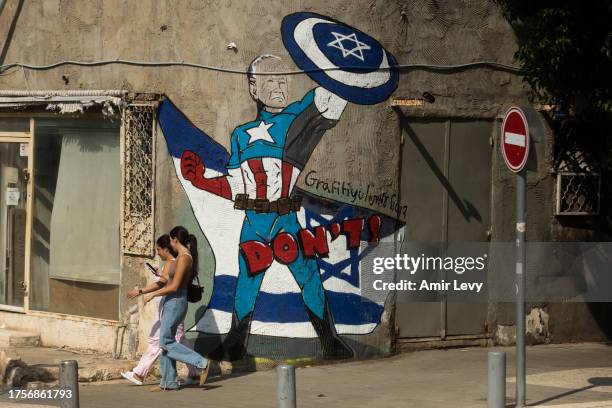 Women walk by street art showing US President, Joe Biden, as Captain America super hero on a street in southern Tel Aviv on November 01, 2023 in Tel...