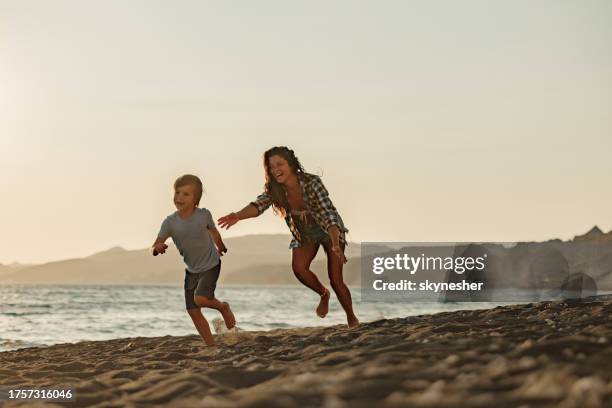 fröhliche alleinerziehende mutter, die ihren sohn am strand jagt. - verfolgen stock-fotos und bilder