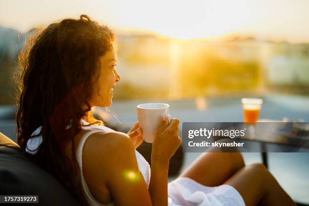 happy woman enjoying in coffee on a patio at sunset. - balcony stock pictures, royalty-free photos & images