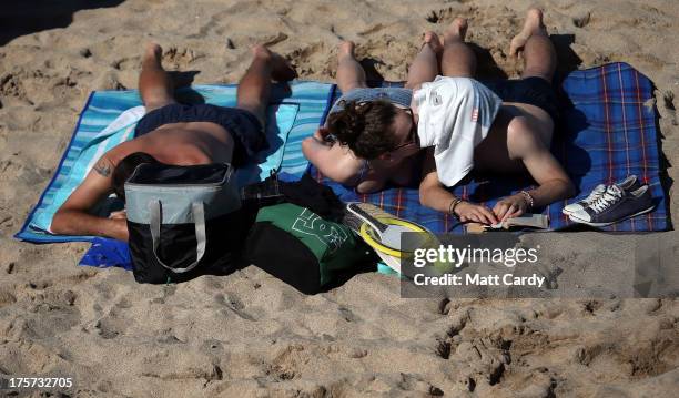 Couple share a kiss as the sunbathe on the beach as the Boardmasters pro-surfing competition takes place on Fistral Beach on August 7, 2013 in...