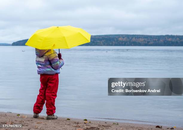 child, caucasian girl, 8 years old, on an autumn walk. a child stands on the shore of a lake with a bright yellow umbrella and dreams while admiring nature. back view. - 8 9 years stock pictures, royalty-free photos & images