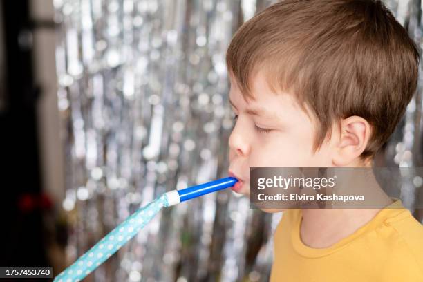 9-year-old boy in a yellow t-shirt blows a whistle at a birthday party against a background of silver sparkles. - blechblasinstrument stock-fotos und bilder