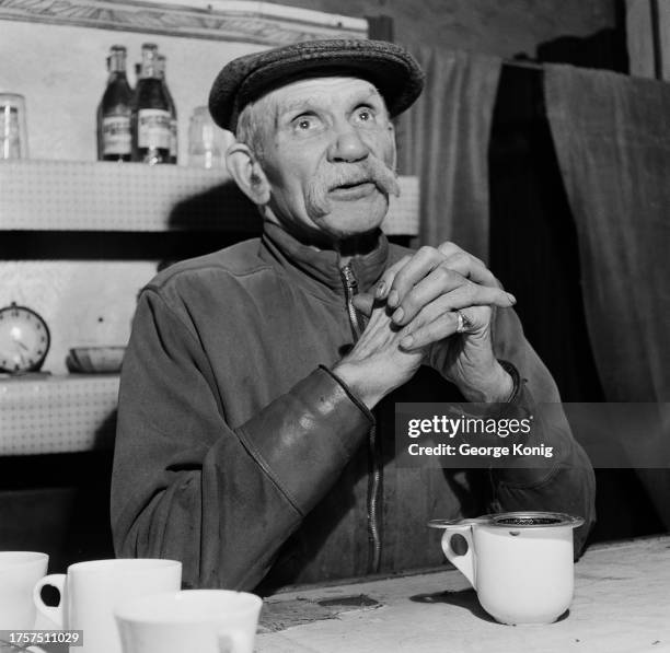 Professor William Klein wearing a flat cap, his elbows resting on the table before him, on which is a mug and tea strainer, at Klein's Olympic Gym in...