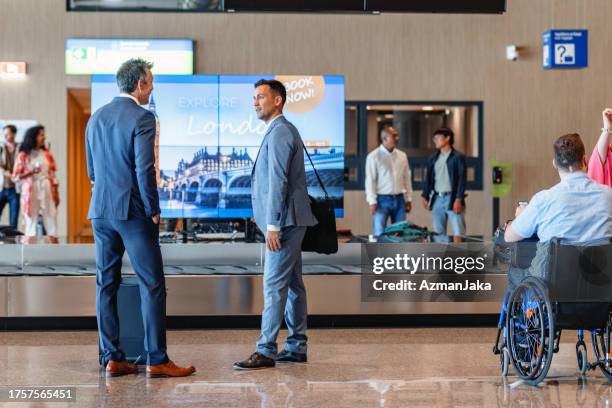 due colleghi d'affari giapponesi in attesa di una valigia all'aeroporto - simbolo internazionale di accesso foto e immagini stock