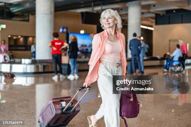 caucasian senior woman smiling while looking for the airport exit - sliding door exit stock pictures, royalty-free photos & images