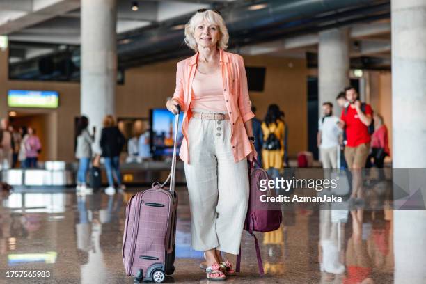 senior woman smiling at the camera while looking for the airport exit - sliding door exit stock pictures, royalty-free photos & images