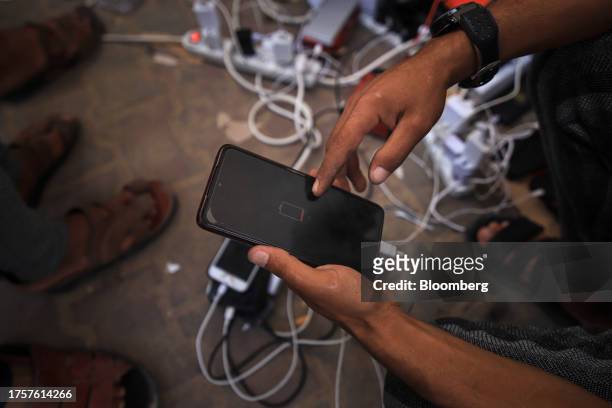 Palestinian man's smartphone shows an empty battery near a portable charging station on a street in western Khan Younis, Gaza, on Tuesday, Oct. 31,...