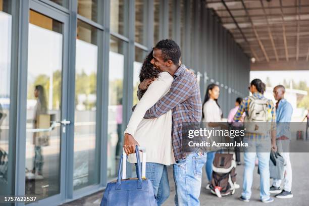 multicultural mid-adult couple hugging at airport departure door - sliding door exit stock pictures, royalty-free photos & images