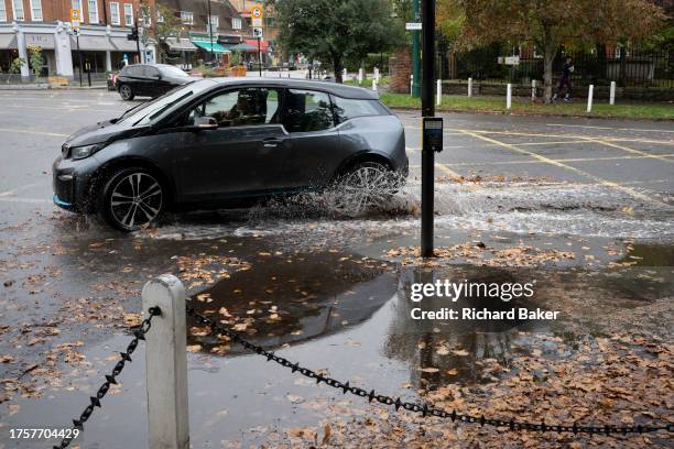 Car turns left and splashes through water and autumn leaves in Dulwich Village, on 1st November 2023, in London, England.