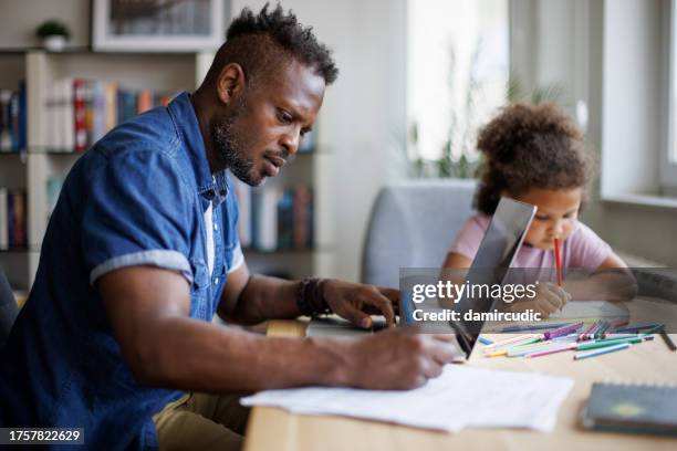 father working on laptop while his daughter drawing beside him at home - preencher um formulário imagens e fotografias de stock