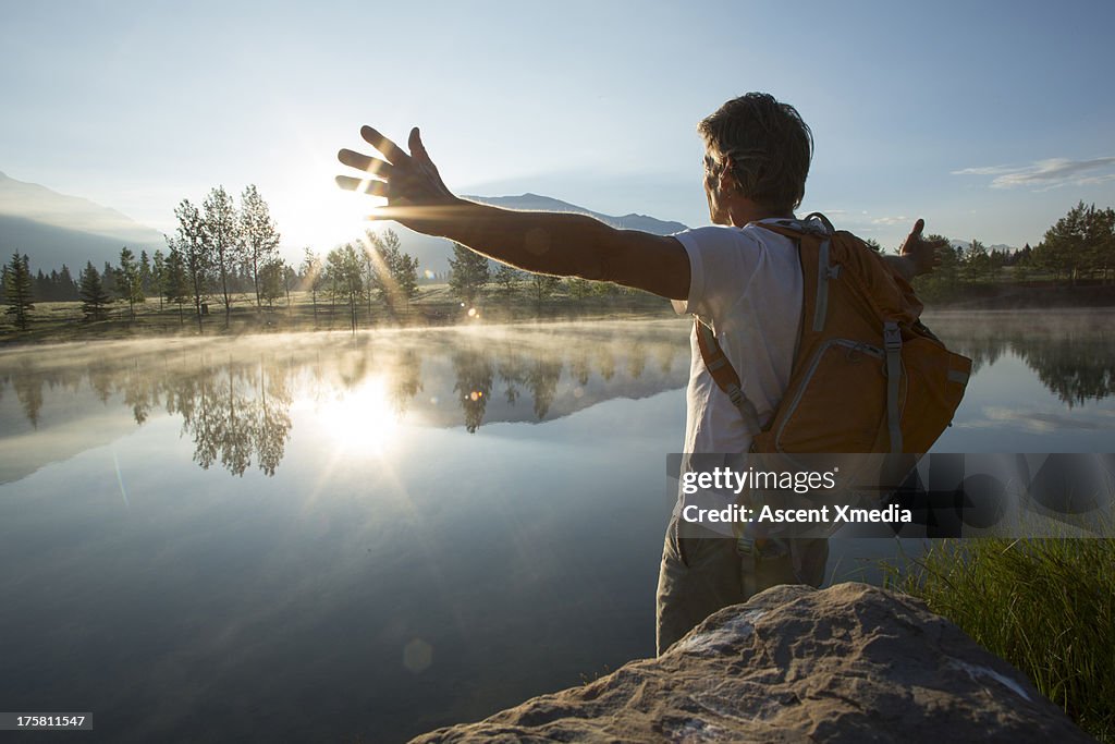 Man spreads arms wide across mountain lake