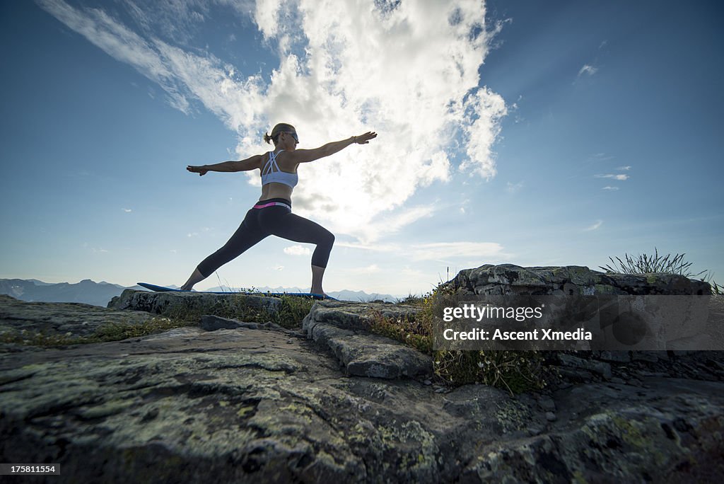 Woman performs yoga moves on bluff above mountains