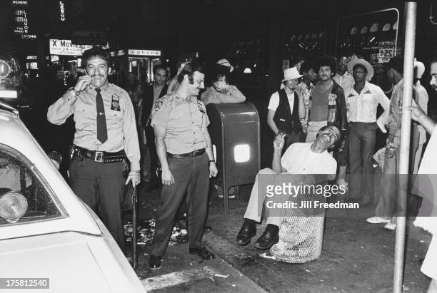 New York police officers find a man sitting in a litter bin in Times Square, New York City, 1976.