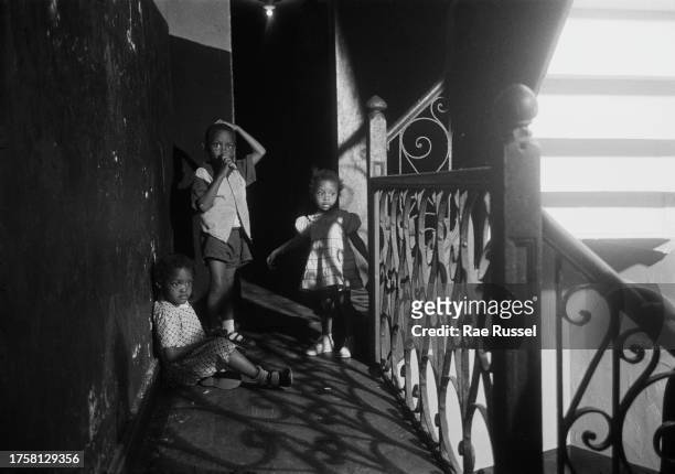 Group of children beside a metalwork balustrade, which casts a shadow on the landing outside a property in a social housing development on Henry...