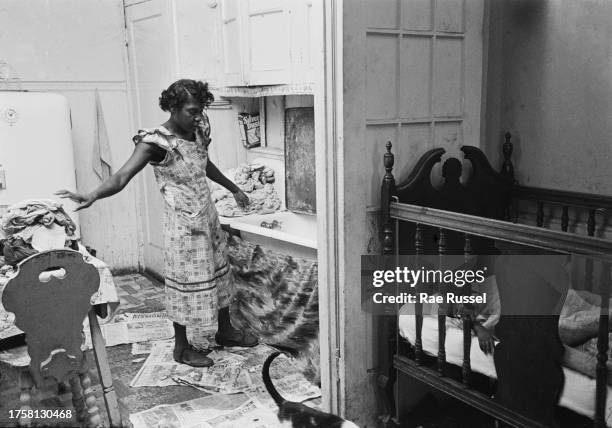 Woman doing the laundry in the kitchen as a child lies in a crib on the other side of the doorway of a property at a social housing development on...