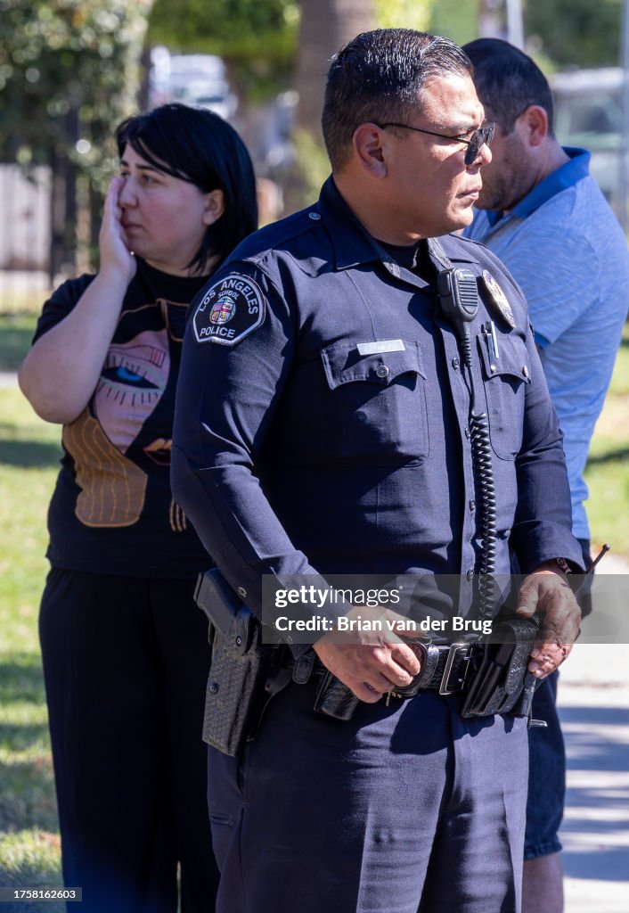 Police officer stands guard with concerned staff and parents