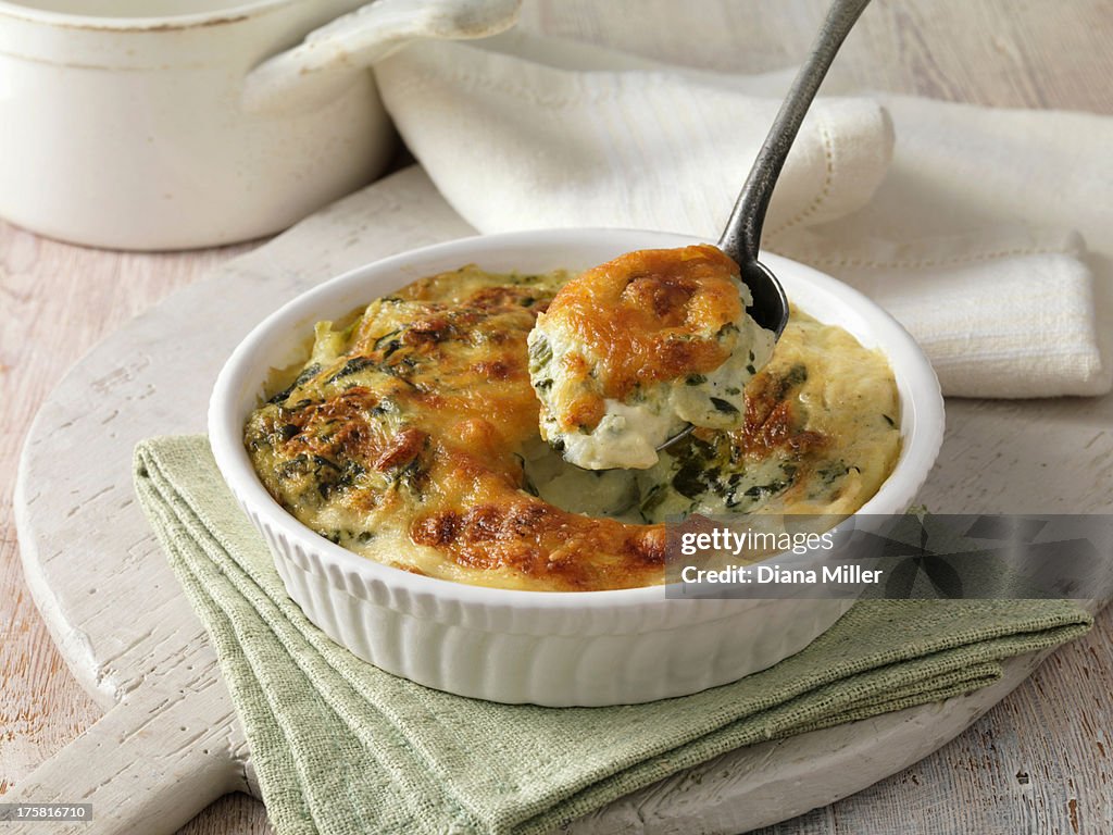 Spinach gratin in a white dish with metal spoon on green cloth