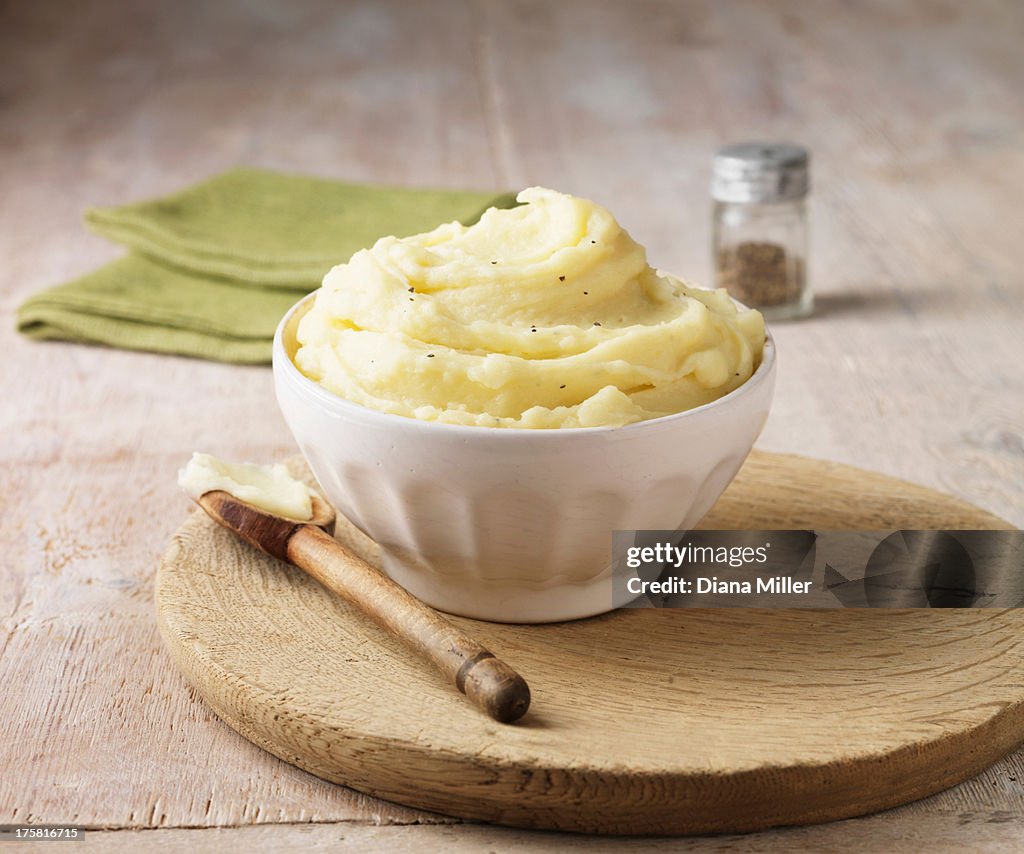 Ultimate mashed potato with black pepper in white faceted bowl with wooden spoon