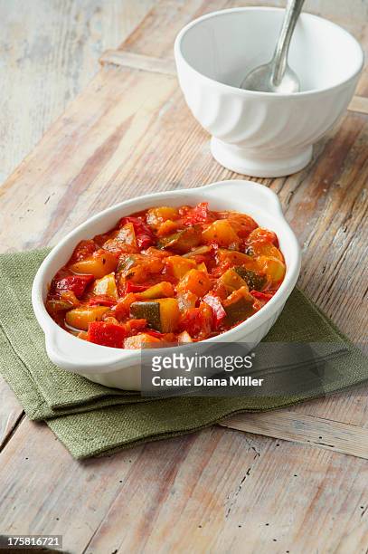 vegetable ratatouille. courgettes, tomatoes and red and yellow peppers in white dish on a green cloth - ratatouille stock pictures, royalty-free photos & images