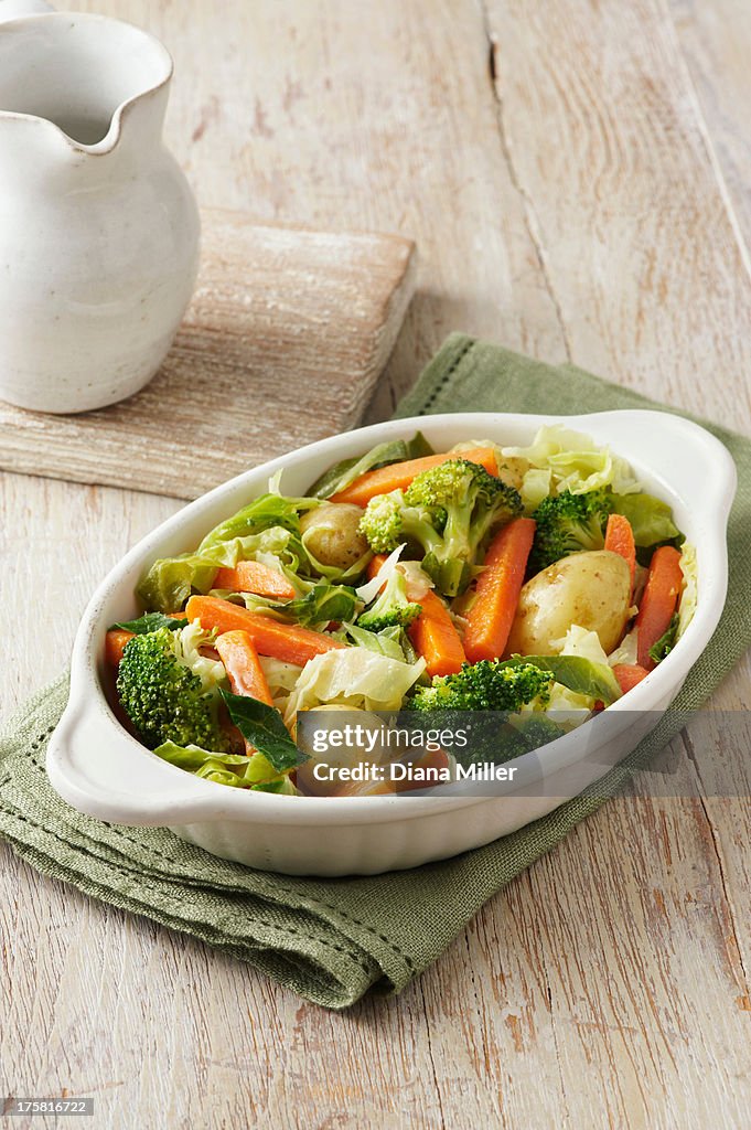 Vegetable selection consisting of broccoli, carrots, new potatoes and cabbage in white serving dish on green cloth