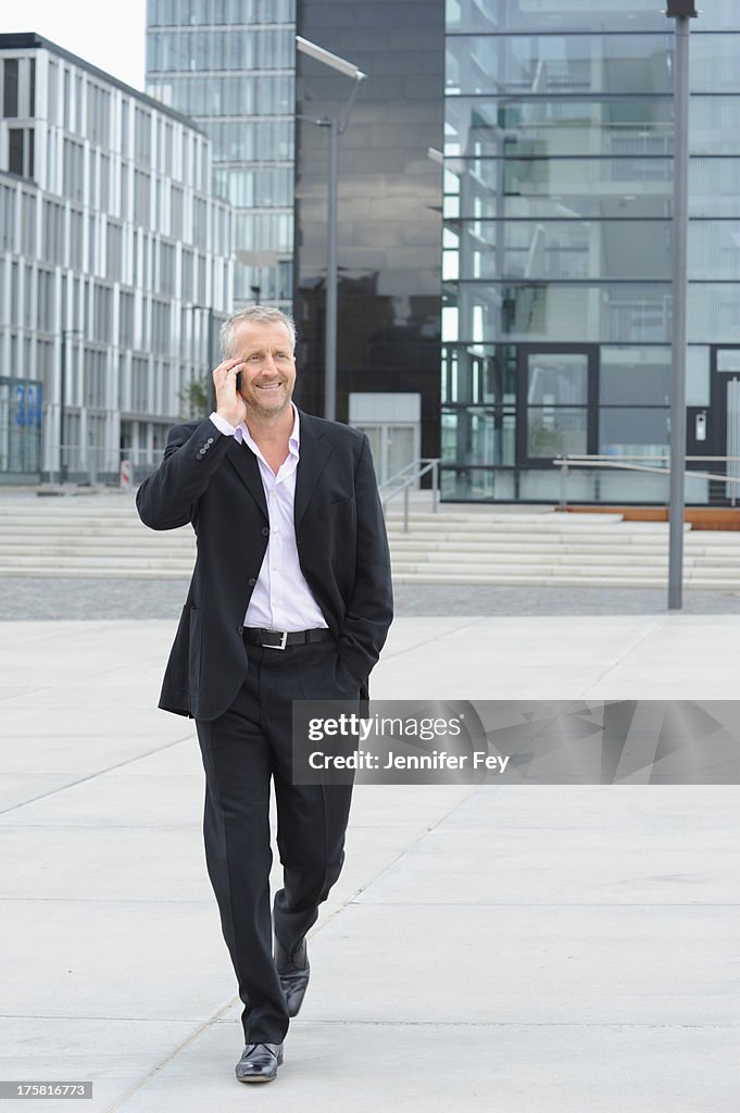 Mature man walking in financial district and using cellphone