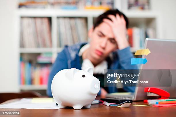 piggy bank with young man worrying in background - deuda estudiantil fotografías e imágenes de stock