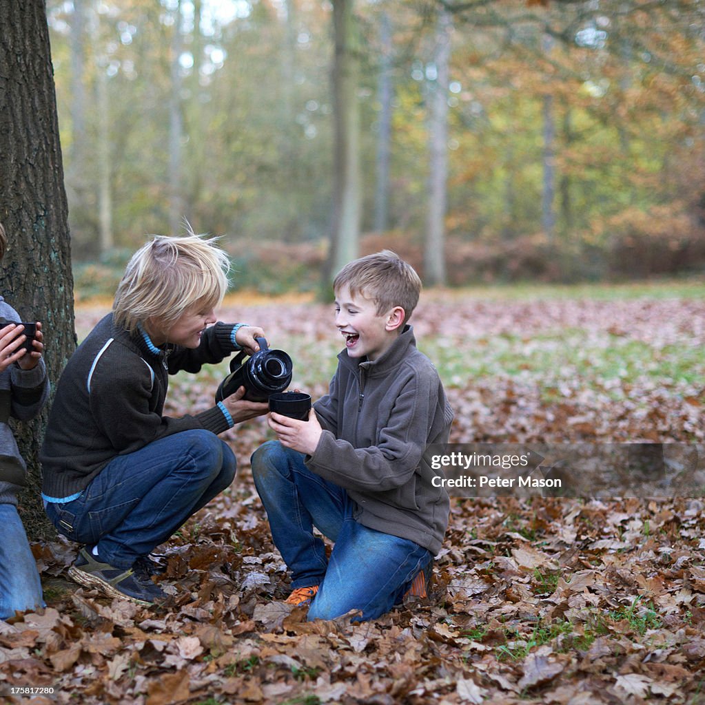 Boys pouring hot drink from flask in forest