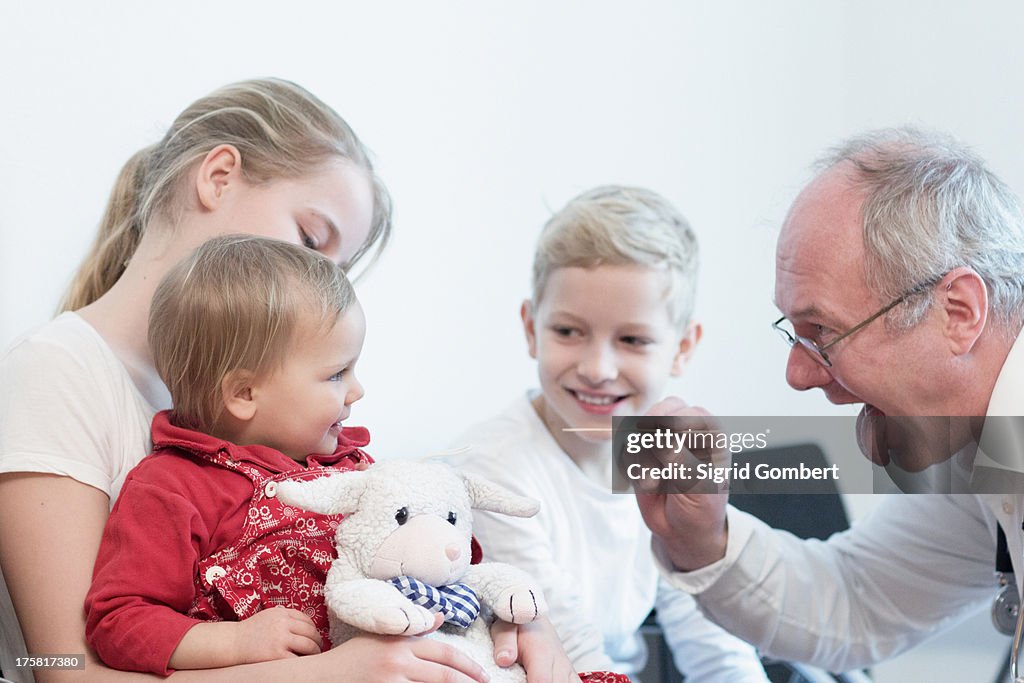 Child on sister's lap being examined by doctor