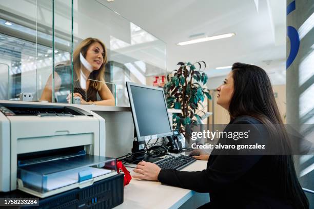 woman at the clinic reception desk talking to the receptionist - secretary stock pictures, royalty-free photos & images