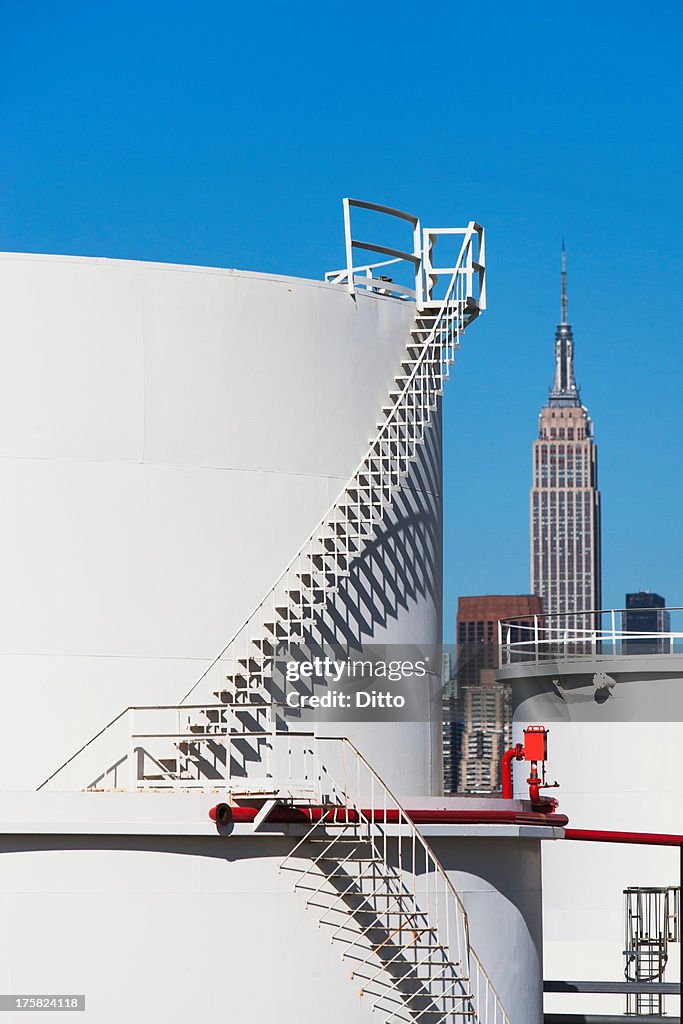 Storage tanks of oil refinery with Empire State building in background, New York, USA