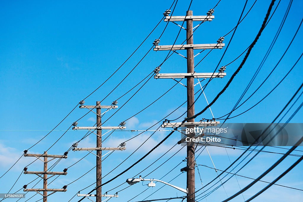 Cables attached to telegraph pole against blue sky